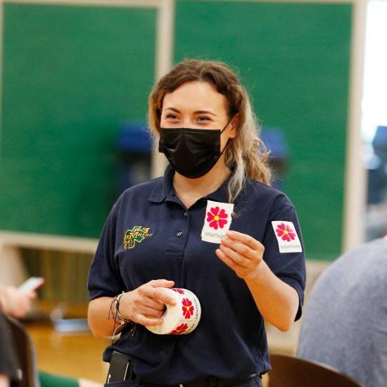 Student wearing a facemask while giving out vaccination stickers 